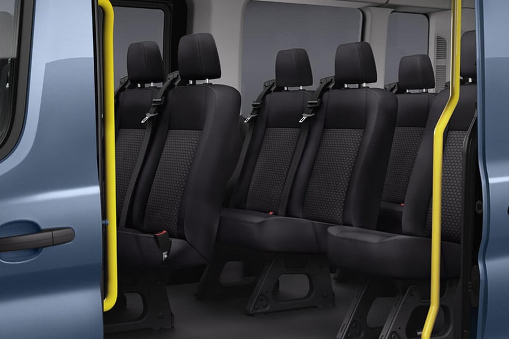 Interiøret i en Ford Transit Minibuss som viser sorte passasjerseter og et gult håndtak nær den åpne døren.